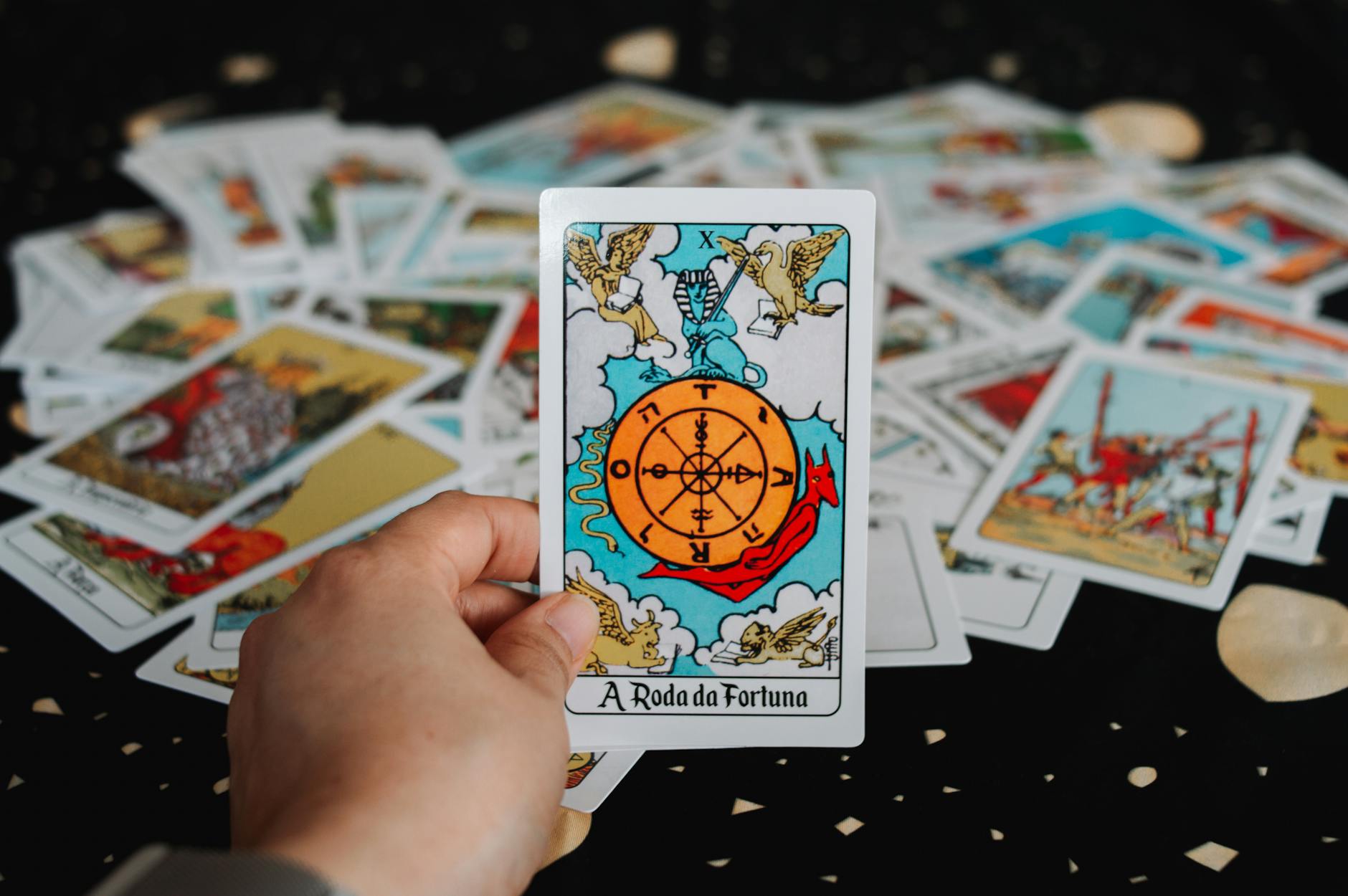 Dłoń trzymająca kartę tarota Koło Fortuny wśród rozrzuconych kart