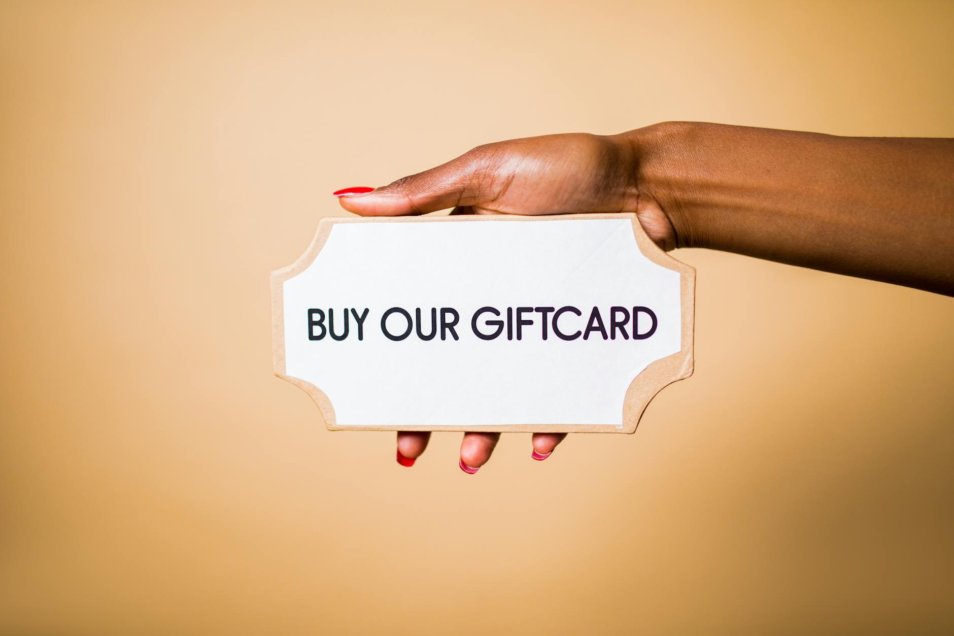 Dłoń trzymająca kartkę z napisem Buy our giftcard na brązowym tle