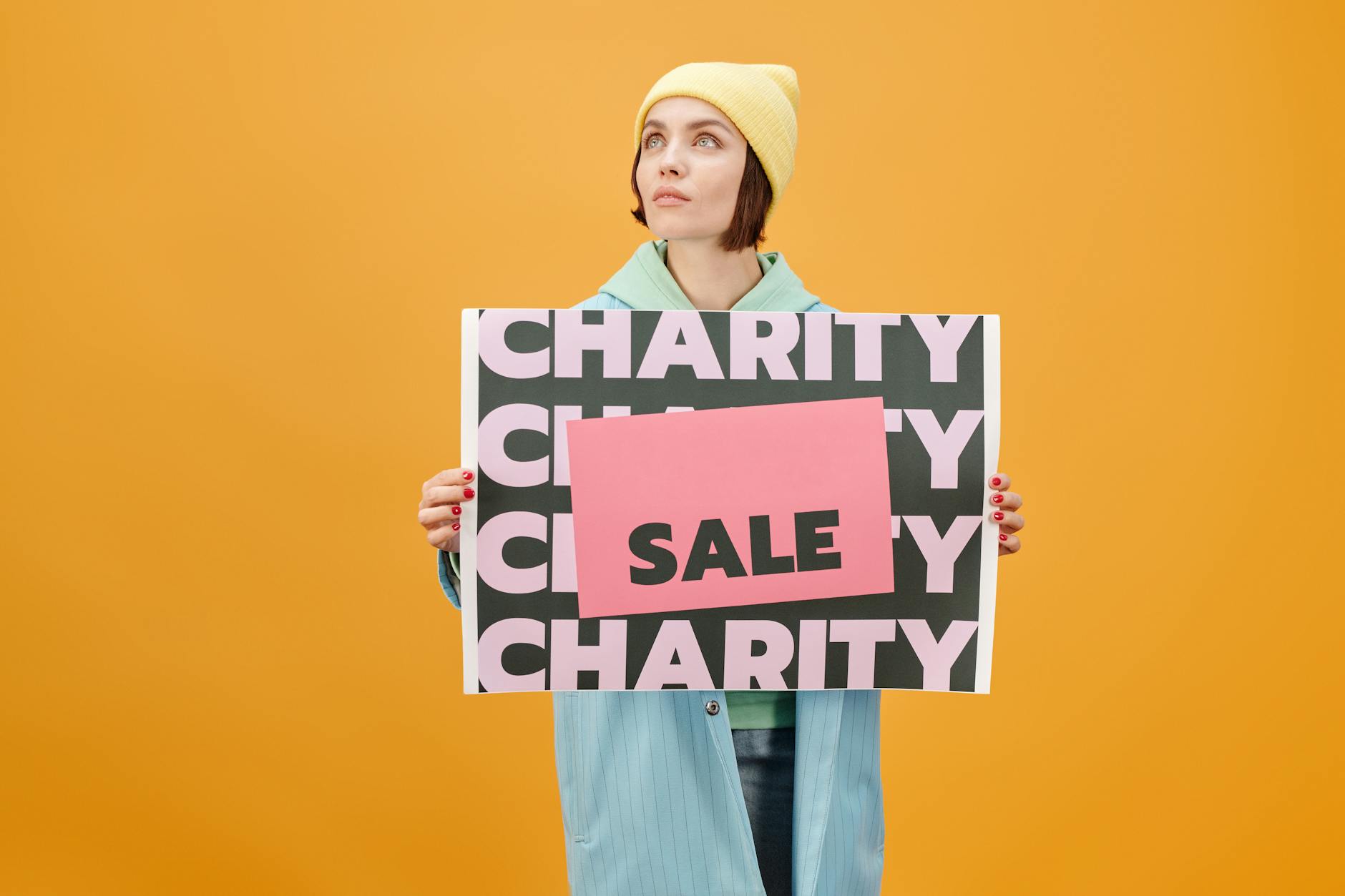 Kobieta w modnym stroju trzymająca tabliczkę charity sale na żółtym tle