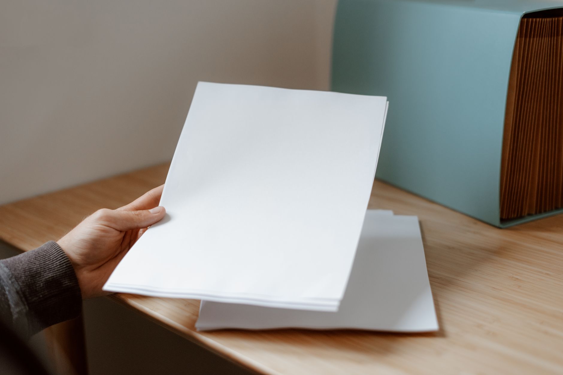 Osoba trzyma pustą kartkę papieru nad drewnianym biurkiem z teczką