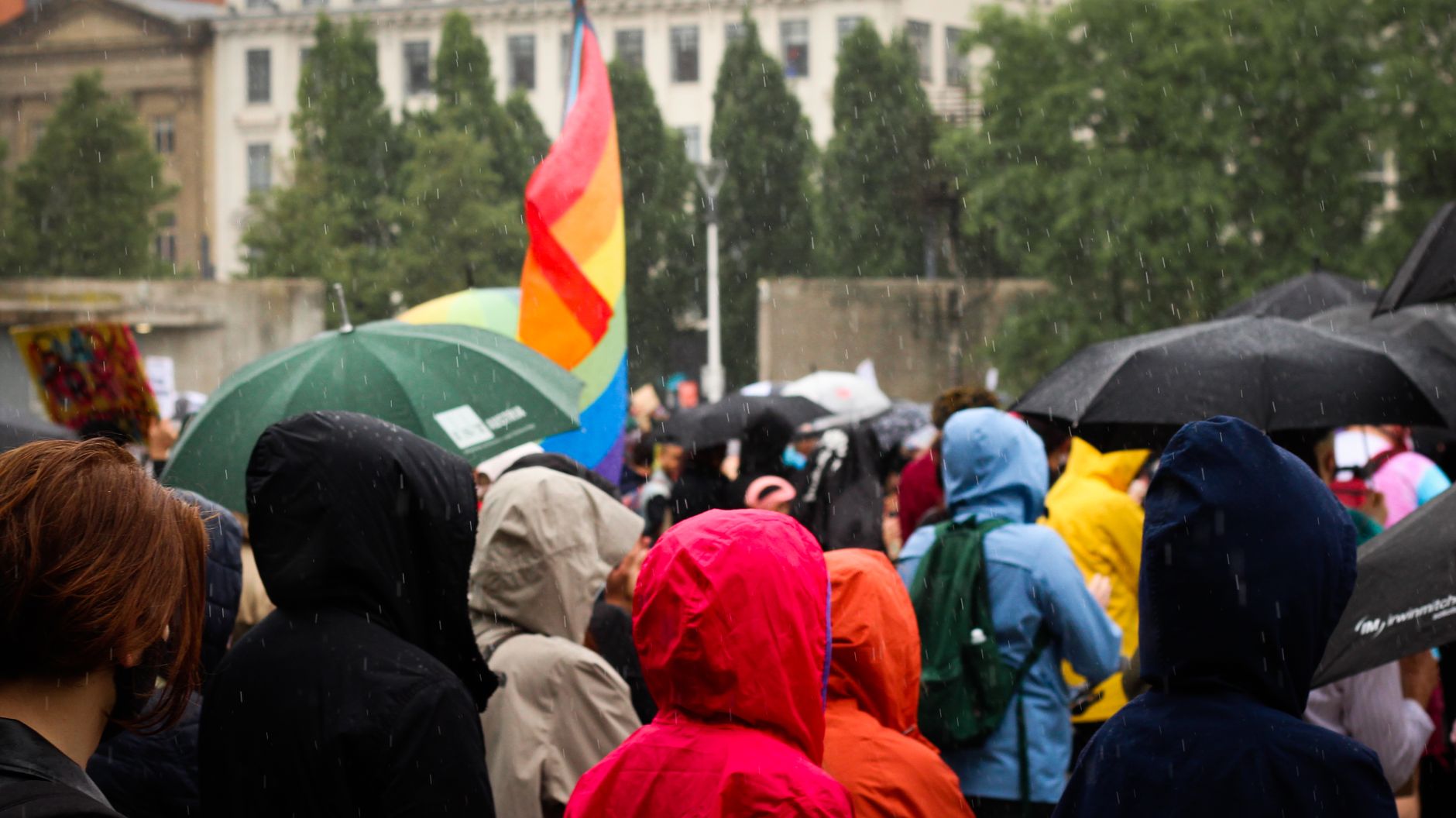 Tęczowa flaga nad tłumem uczestników marszu w deszczu